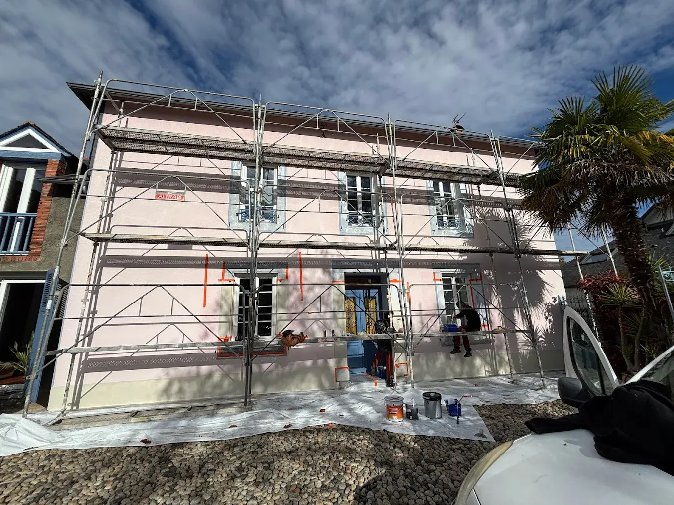 Façade de maison avant ravalement : sous-couche claire et repérages, échafaudage monté et peintres au travail
